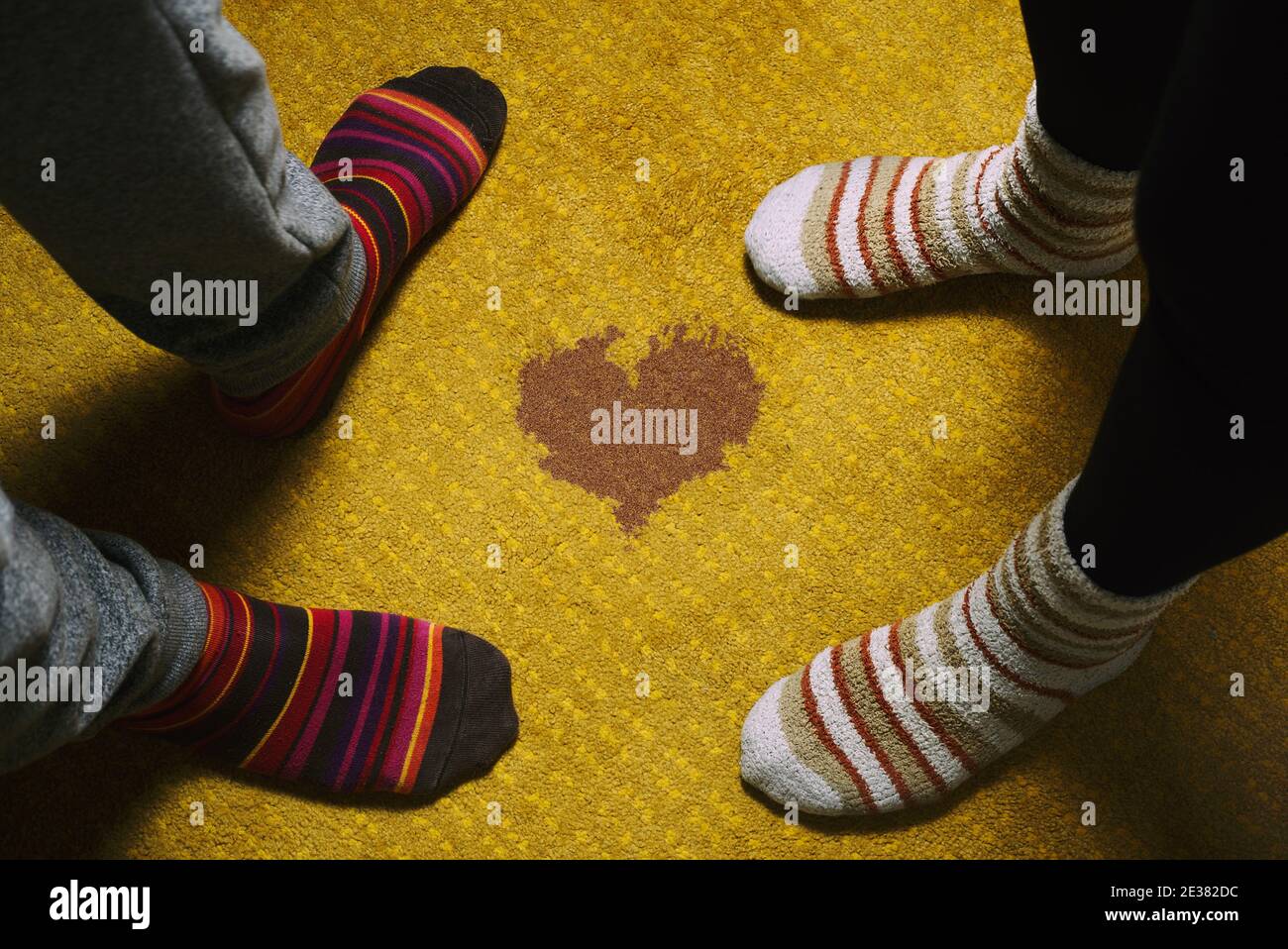 amore e giorno di san valentino. piedi di donna e uomo con calze colorate su tappeto giallo e macchia a forma di cuore. Foto Stock