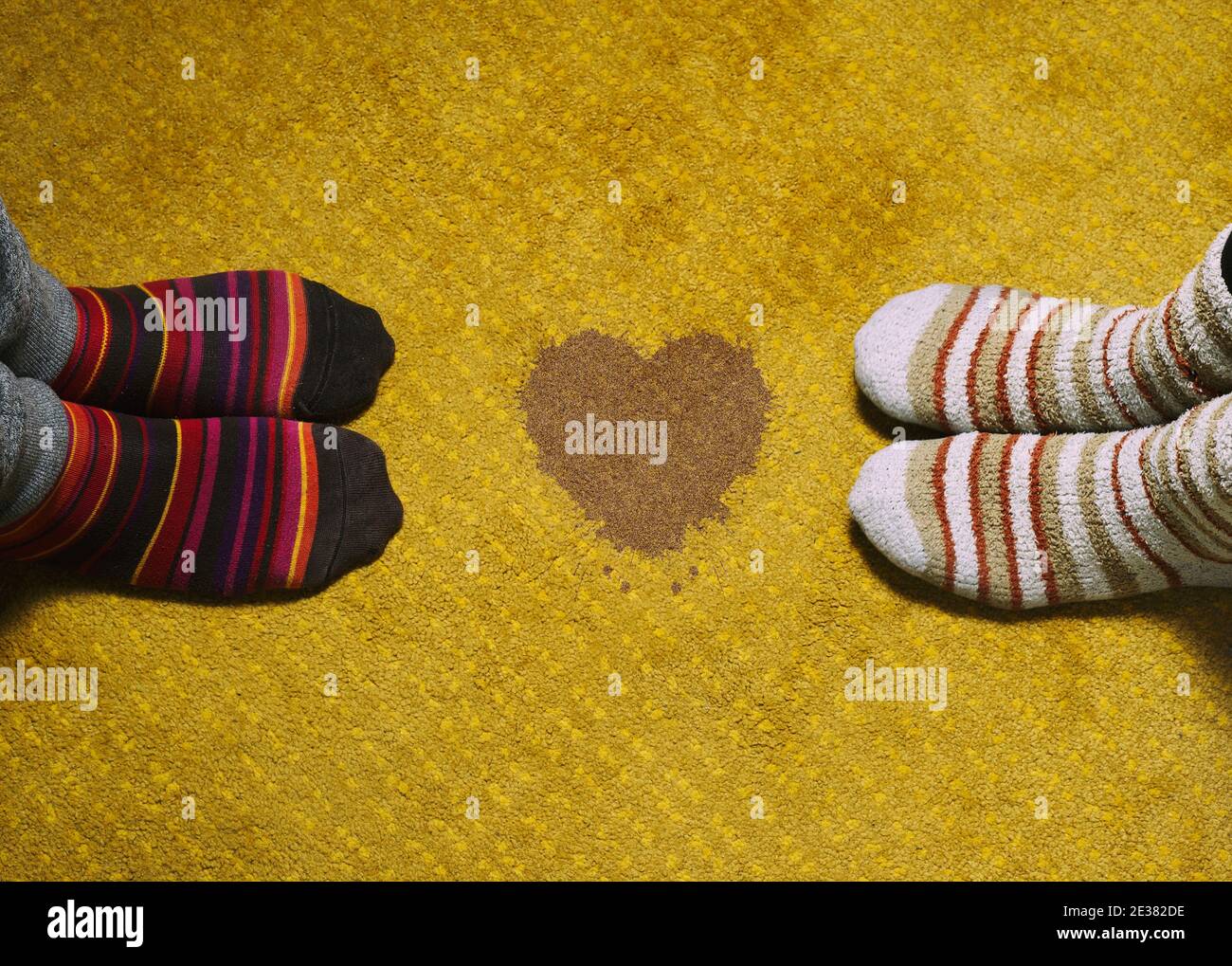 amore e giorno di san valentino. piedi di donna e uomo con calze colorate su tappeto giallo e macchia a forma di cuore. Foto Stock