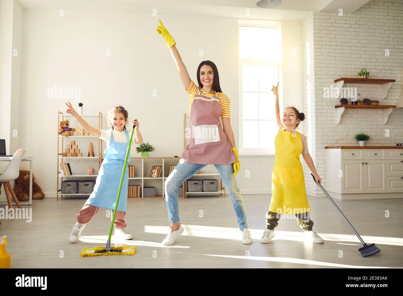 Felici i bambini e le giovani madri che ballano e si divertono durante la pulizia del pavimento Foto Stock