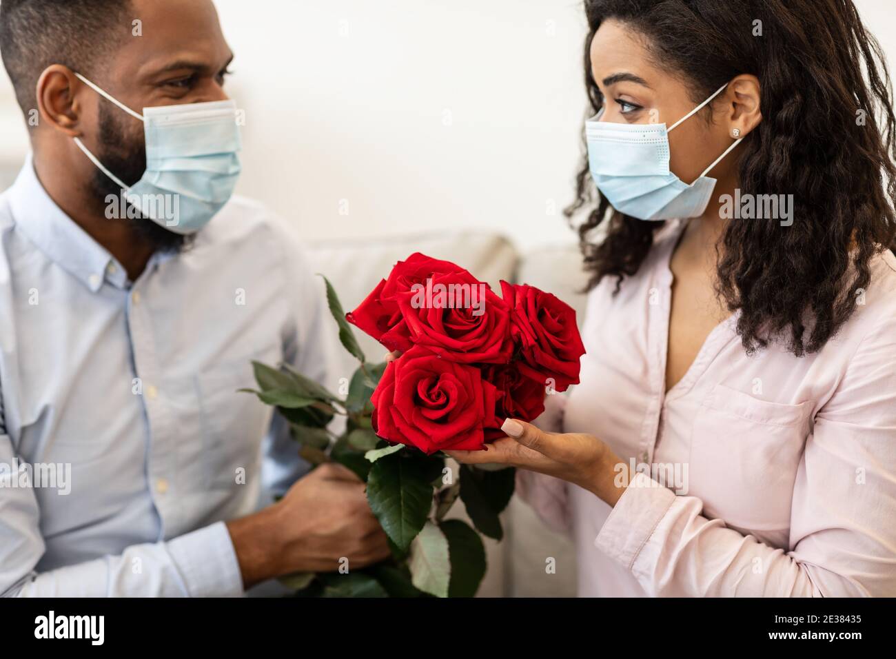 Coppia nera in maschere mediche con data, tenendo rose Foto Stock