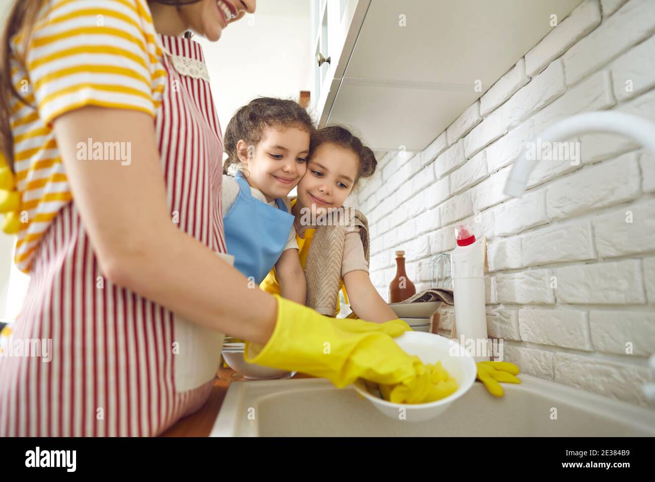 Due ragazze imparano a fare le faccende domestiche e a guardare la madre lavare i piatti dopo pranzo Foto Stock