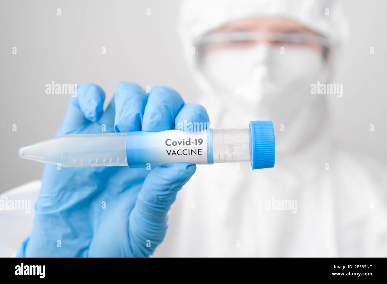 Medico che indossa tuta monouso o tuta protettiva con maschera e sicurezza google che tiene una provetta con vaccino. Foto Stock