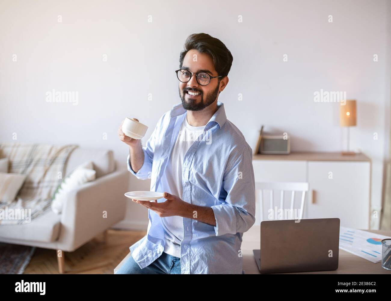 Vantaggi del lavoro a distanza. Happy Arab Freelancer Guy bere caffè presso l'ufficio domestico Foto Stock