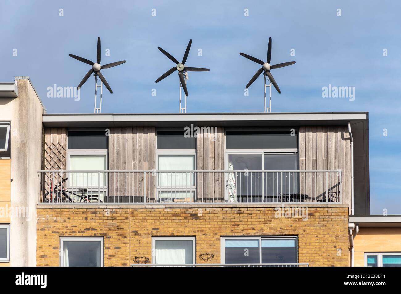 Tre piccole turbine eoliche sul tetto di un blocco di appartamenti o appartamenti residenziali, Regno Unito. Energia sostenibile, sostenibilità. Foto Stock