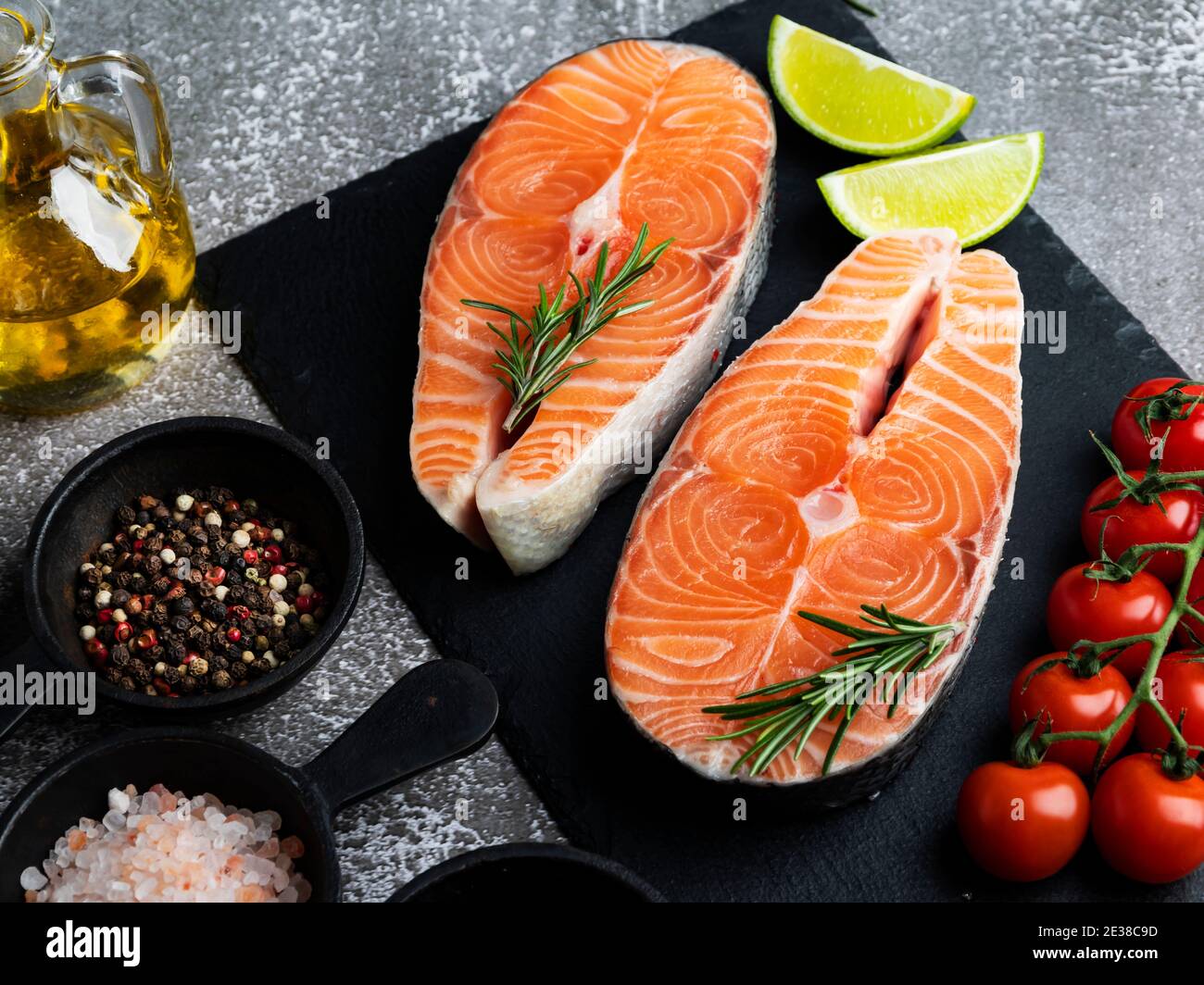 due trote crude di pesce bistecca, salmone e spezie su una superficie di pietra nera, scura Foto Stock