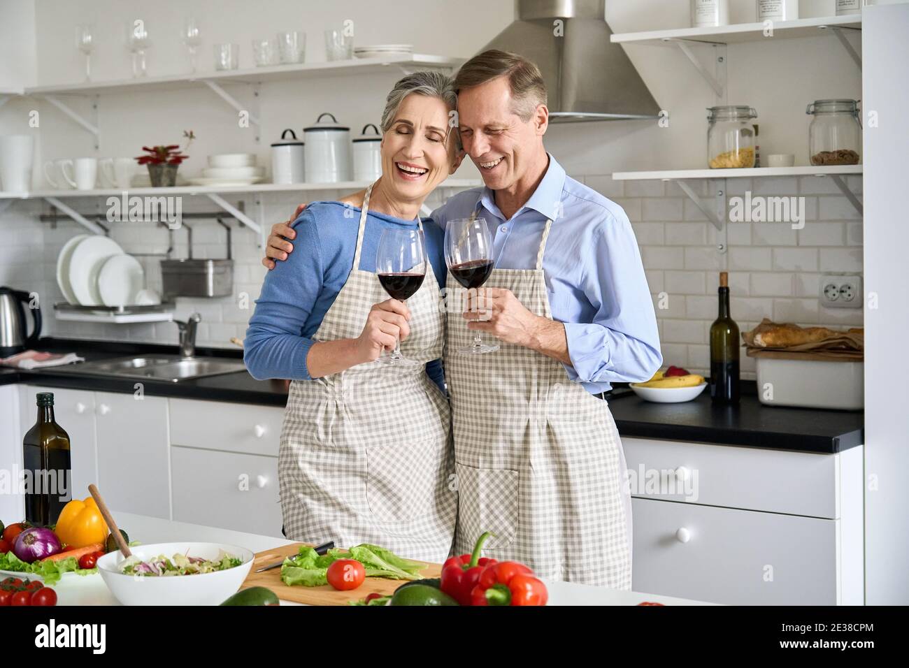 Felice vecchia coppia bere vino preparare insalata di verdure in cucina a casa. Foto Stock