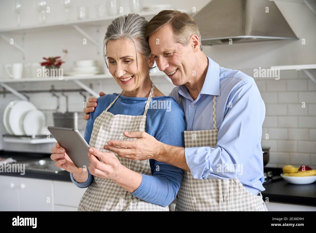 Felice vecchia coppia usando il tablet facendo shopping di drogheria in linea a casa in cucina. Foto Stock