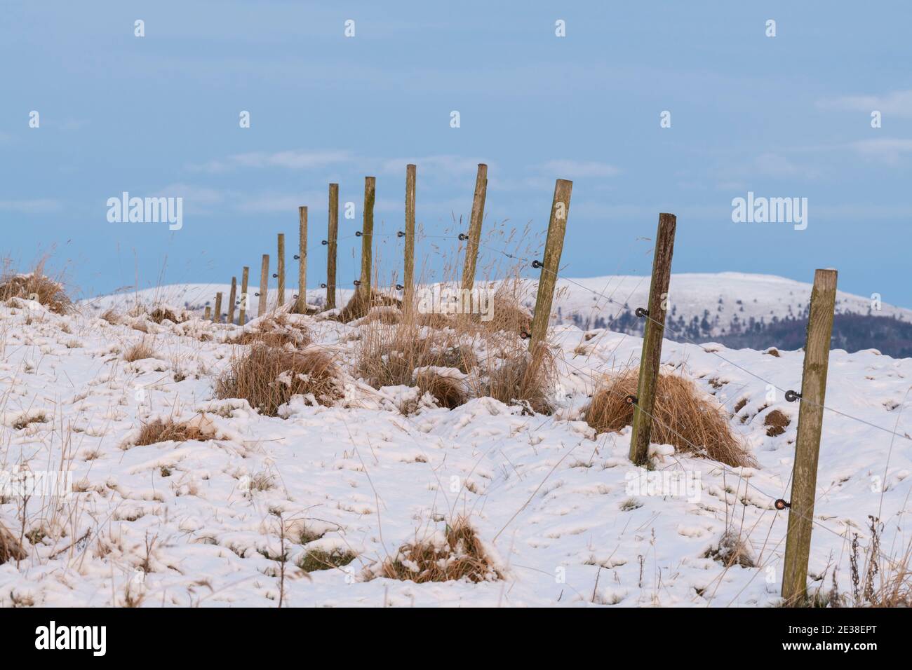 Neve coperta radente con una recinzione elettrica che si arriccia sopra Hillside verso l'orizzonte Foto Stock