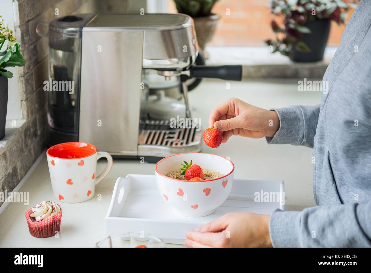 Donna che aggiunge la frutta di fragola alla ciotola di porridge di farinata d'avena. Preparare una colazione a sorpresa per gli amanti il giorno di San Valentino. Semplice idea di cibo sano e festivo Foto Stock