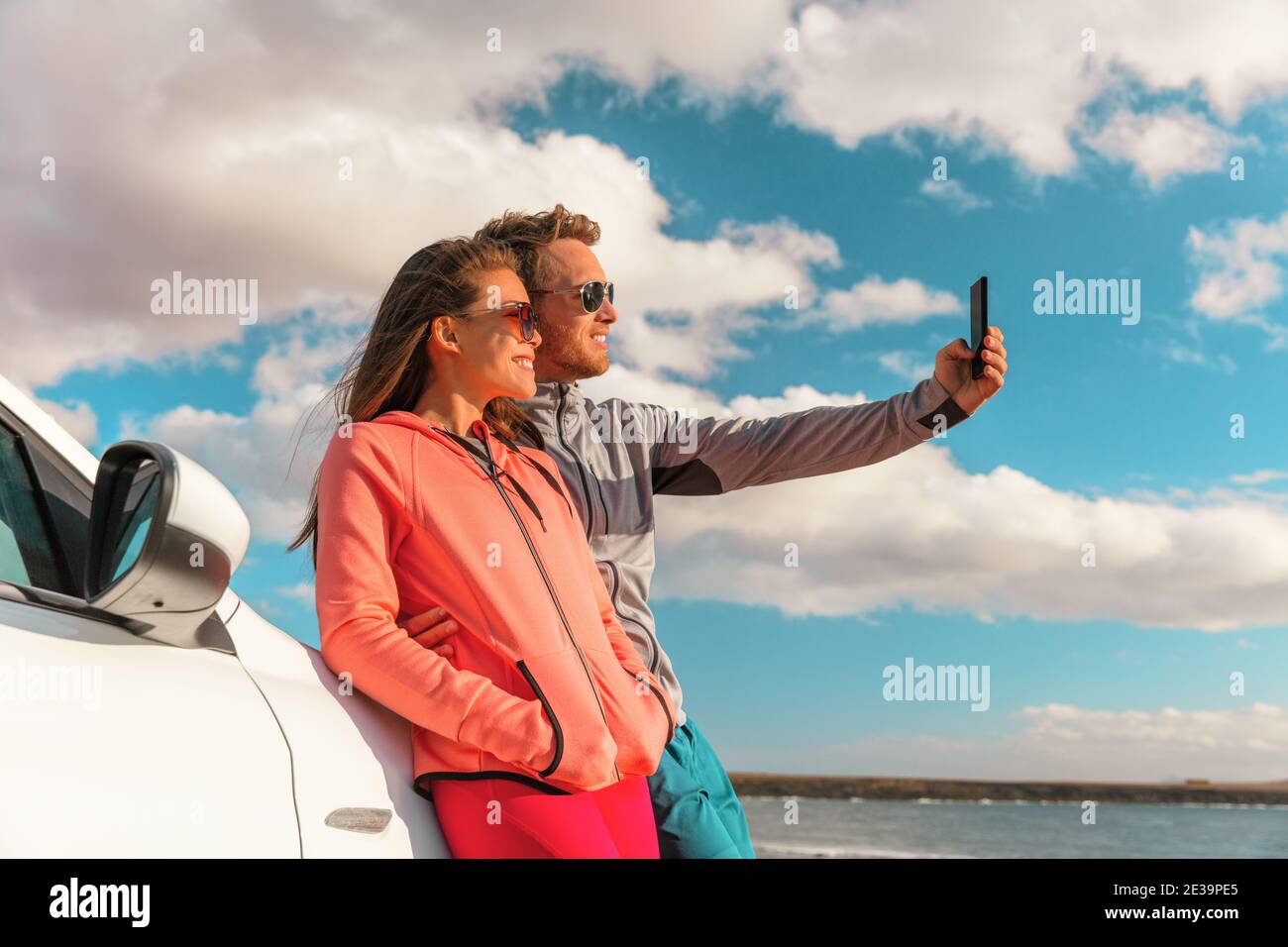 Coppie di selfie turisti in viaggio di strada scattando foto con il telefono al noleggio di auto di vacanza estate. Giovane donna e amico uomo sorridente in occhiali da sole Foto Stock