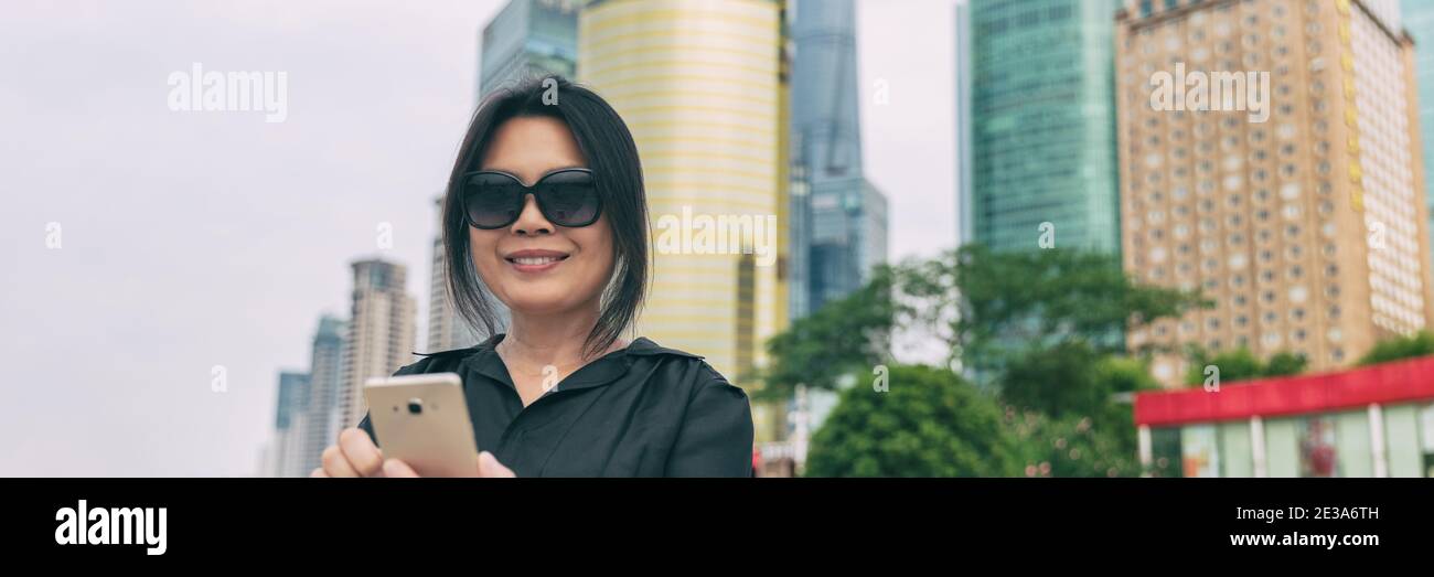 Telefono Asian donna matura che viaggia utilizzando un dispositivo mobile 5g per viaggi di lavoro viaggio città stile di vita banner panoramico. Elegante signora cinese con Foto Stock