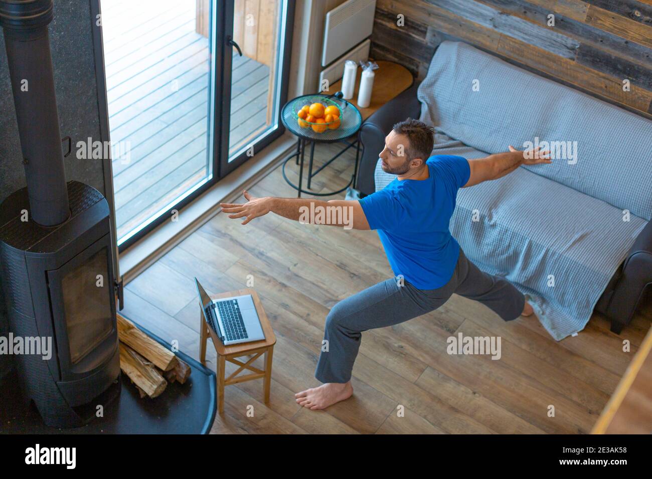 Un uomo lavora a casa online di fronte a un monitor portatile. Pilates, yoga e concetto di stile di vita sano. Posa dell'arciere. Foto Stock