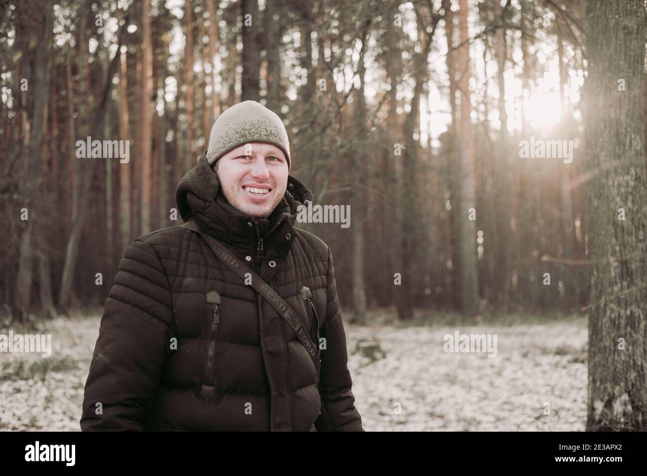 Uomo sorridente nella foresta invernale. L'uomo felice cammina nella foresta innevata. Un ragazzo di buon umore. Escursione attraverso la foresta invernale. Viaggio invernale. Natura wal Foto Stock