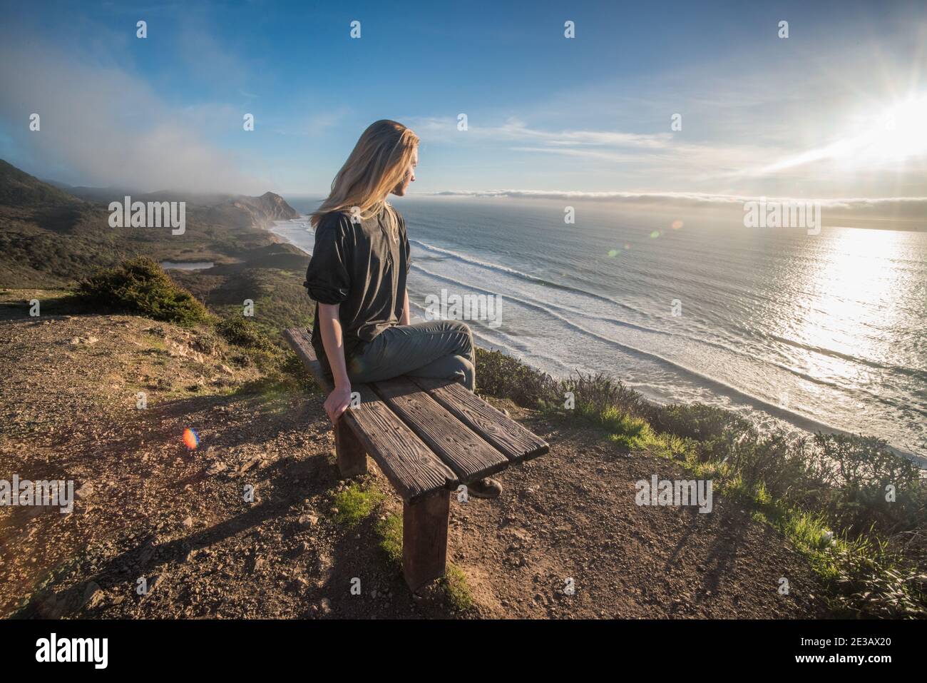 Un biondo escursionista si trova su una panchina che si affaccia sull'oceano pacifico in una splendida porzione della costa californiana in riva al mare nazionale di Point Reyes. Foto Stock