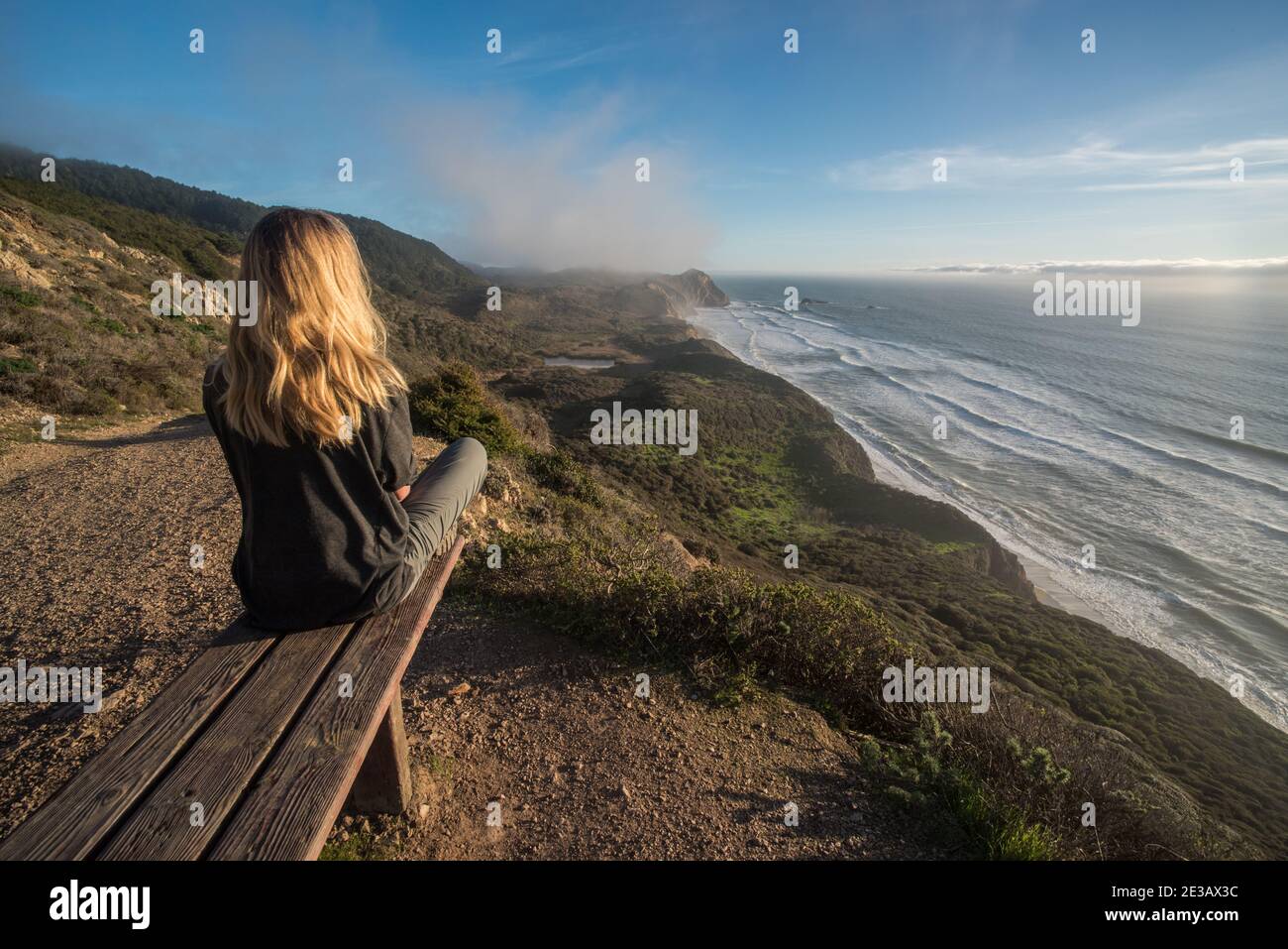 Un biondo escursionista si trova su una panchina che si affaccia sull'oceano pacifico in una splendida porzione della costa californiana in riva al mare nazionale di Point Reyes. Foto Stock Un biondo escursionista si trova su una panchina che si affaccia sull'oceano pacifico in una splendida porzione della costa californiana in riva al mare nazionale di Point Reyes. Foto Stock