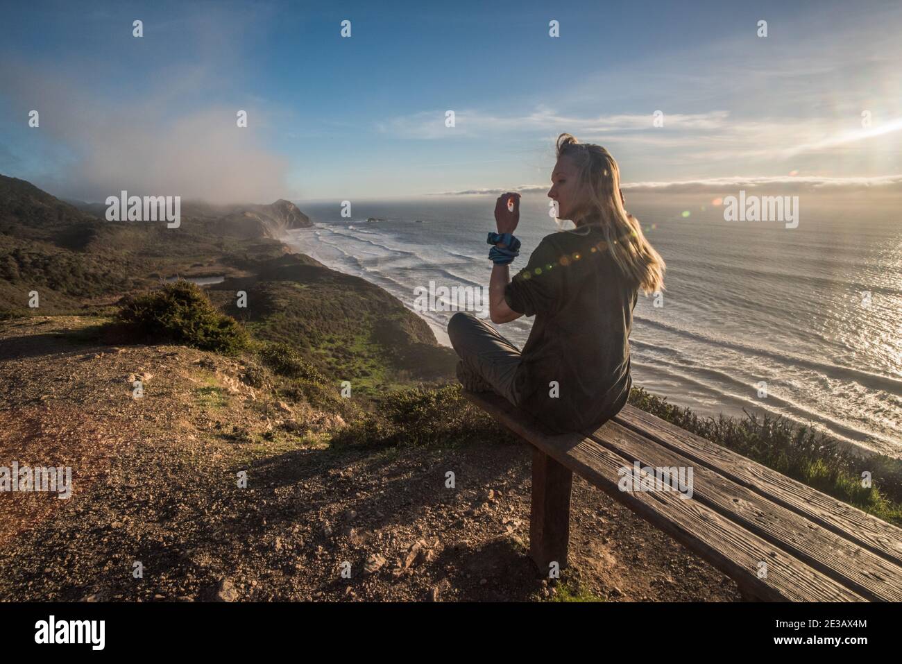 Un biondo escursionista si trova su una panchina che si affaccia sull'oceano pacifico in una splendida porzione della costa californiana in riva al mare nazionale di Point Reyes. Foto Stock