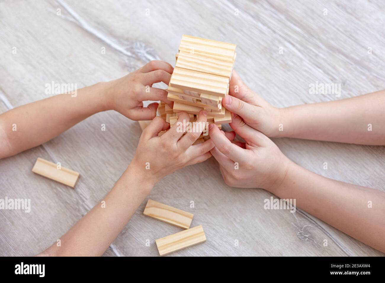 Le mani dei bambini raccolgono una torre di blocchi di legno sul pavimento. Foto Stock