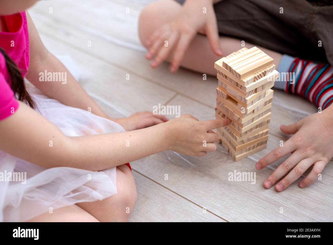 Le mani dei bambini raccolgono una torre di blocchi di legno sul pavimento. Foto Stock