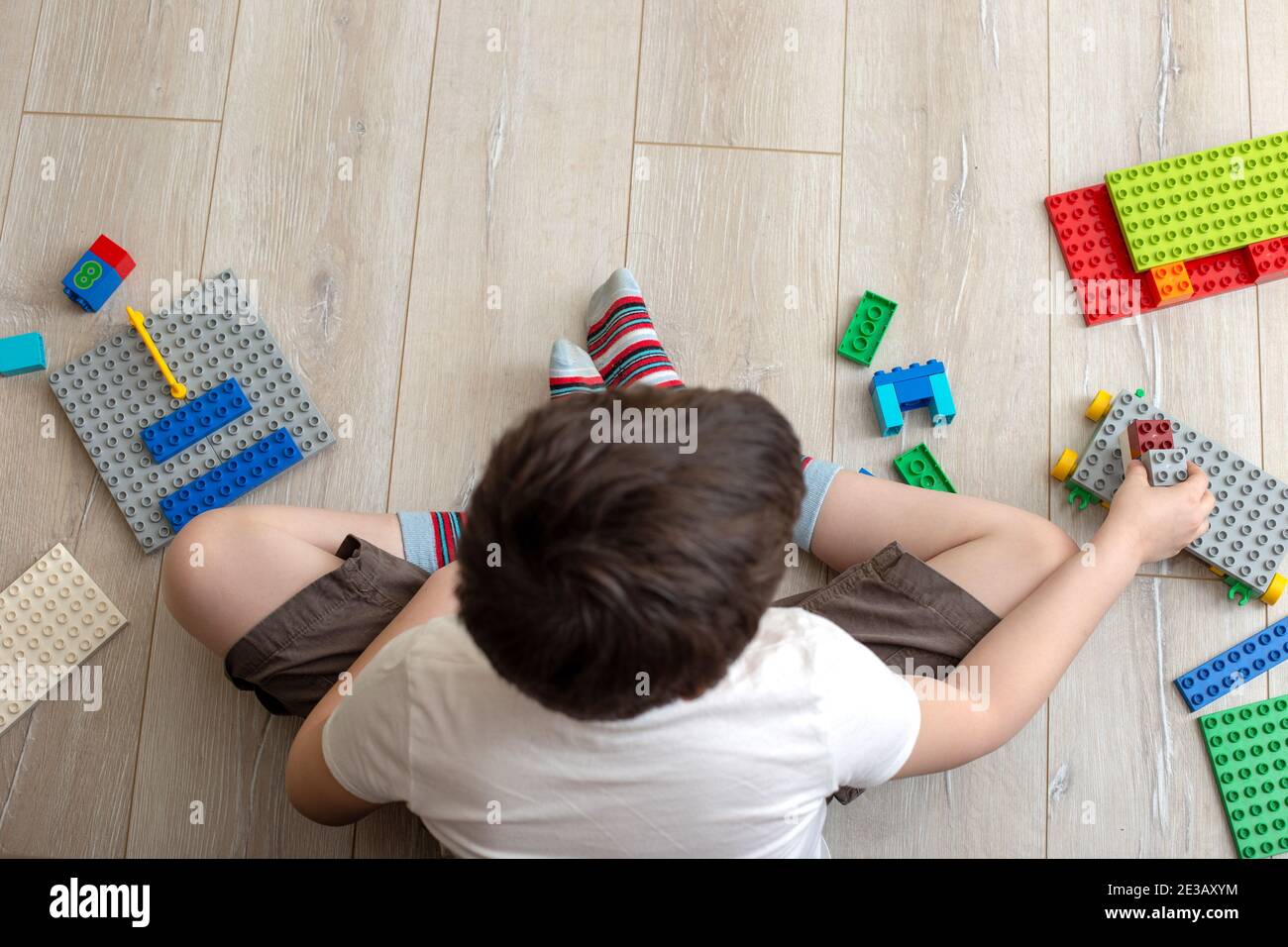 Gioco di ragazzo con costruttore di plastica multicolore sul pavimento in camera. Vista dall'alto Foto Stock