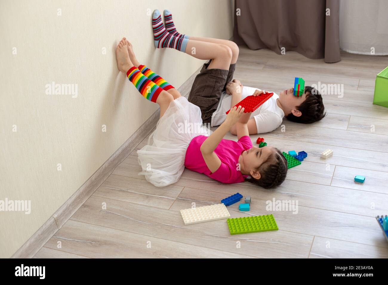 Bambini divertenti, fratello e sorella, stanno sdraiati sul pavimento e giocano nella costruzione di plastica Foto Stock