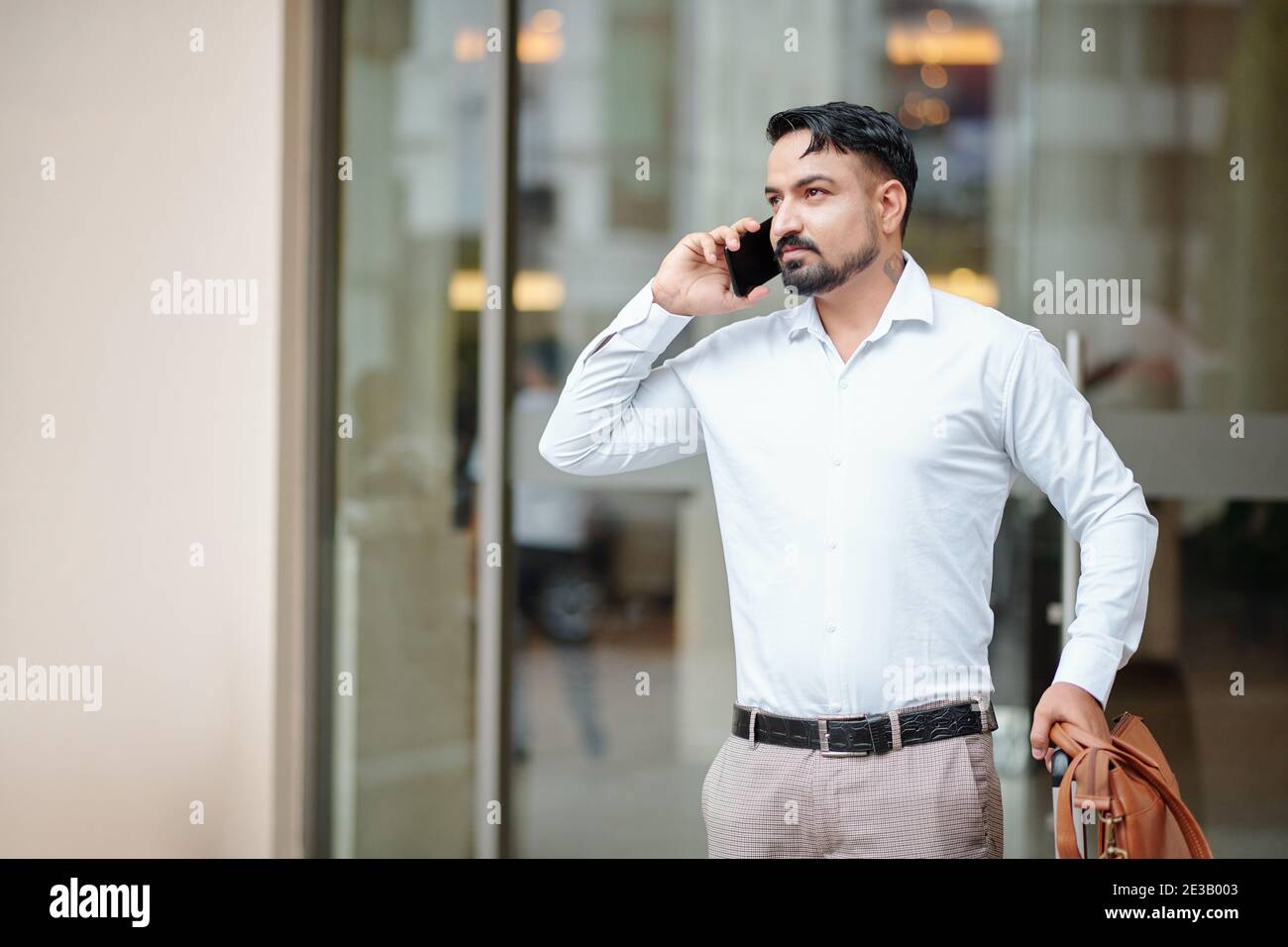 Bell'uomo con valigia e borsa in pelle che parla al telefono in attesa di  un taxi all'ingresso dell'hotel Foto stock - Alamy