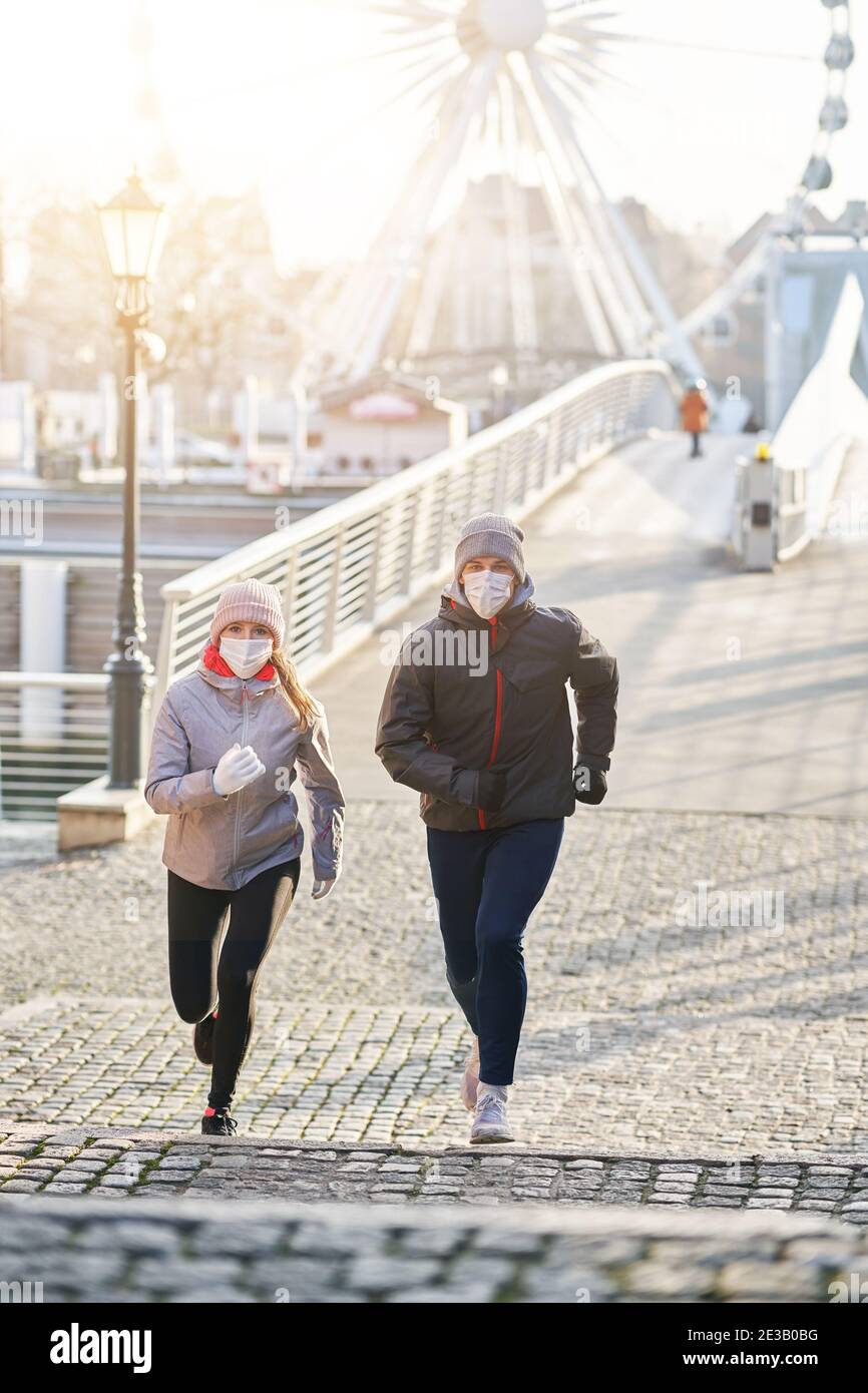 Coppia adulta che fa jogging in città in maschere durante il blocco Foto Stock