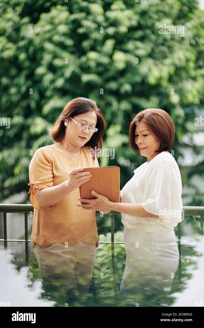 Senior vietnamita femmina amici in piedi all'aperto e discutere articolo su computer tablet Foto Stock