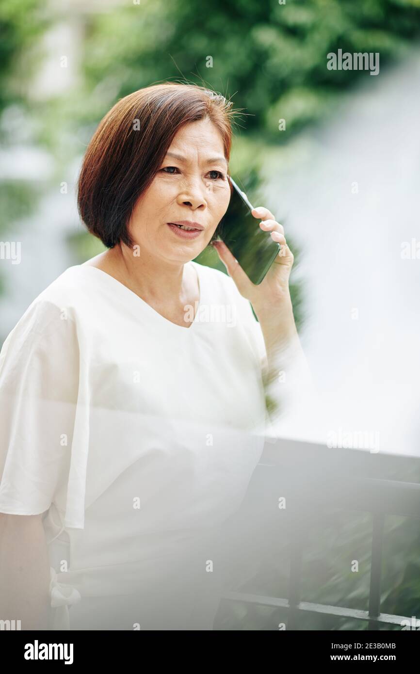 Ritratto della donna asiatica anziana seria che parla al telefono con amico o familiare Foto Stock