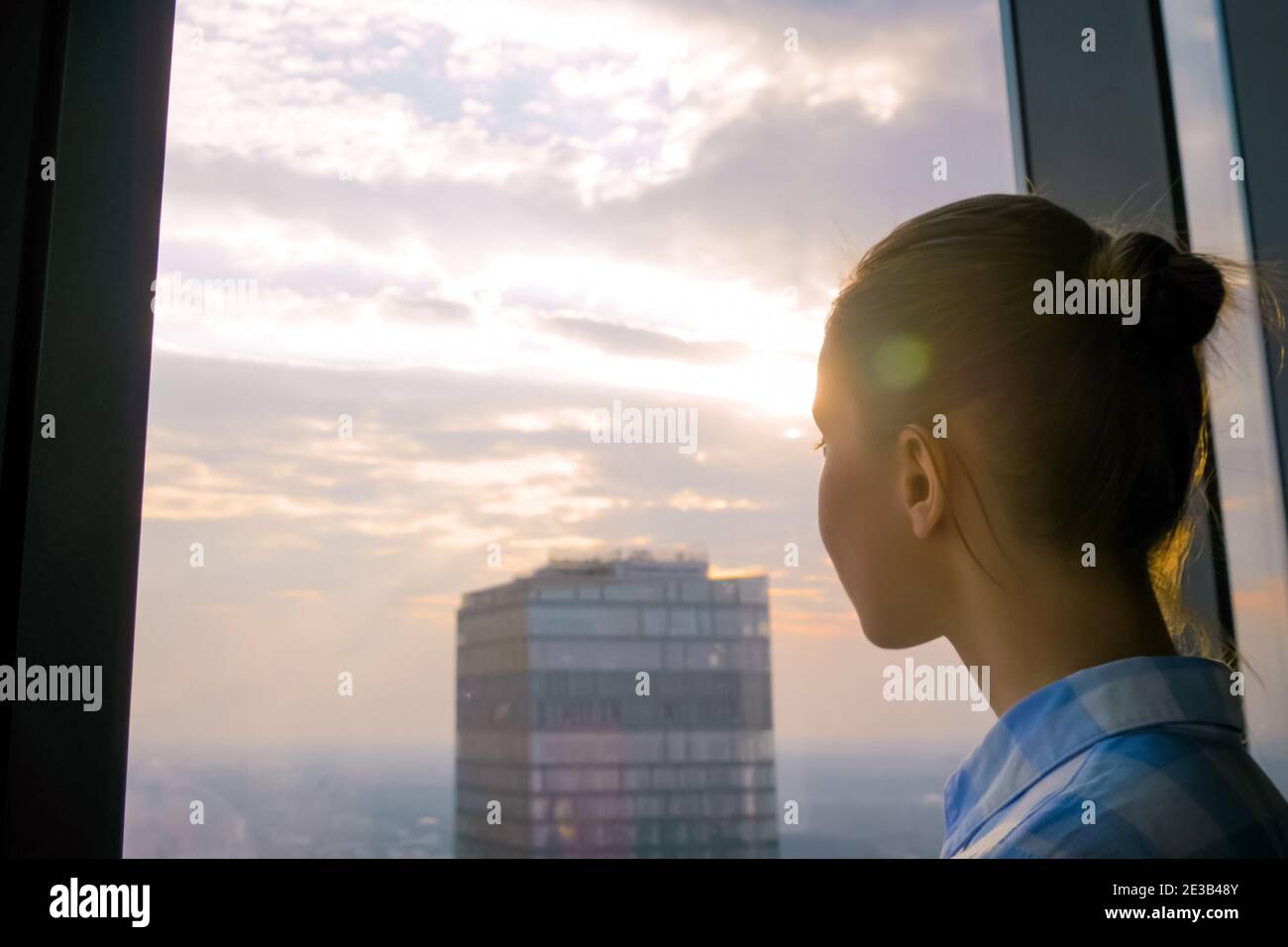 Donna che guarda il paesaggio urbano attraverso la finestra del grattacielo - sole svasatura lente Foto Stock