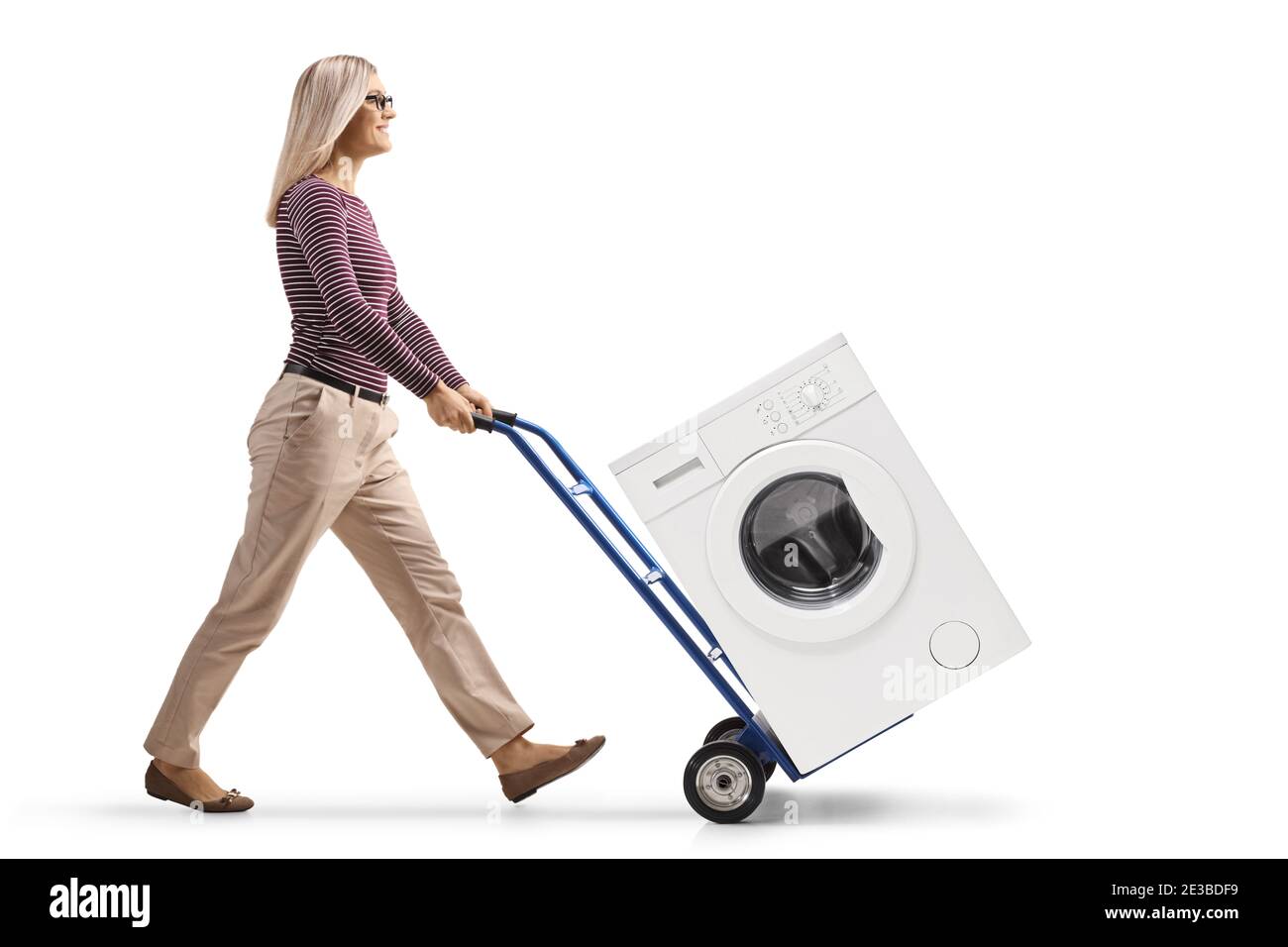 Foto di profilo a lunghezza intera di una giovane donna che spinge un lavatrice con carrello isolato su fondo bianco Foto Stock