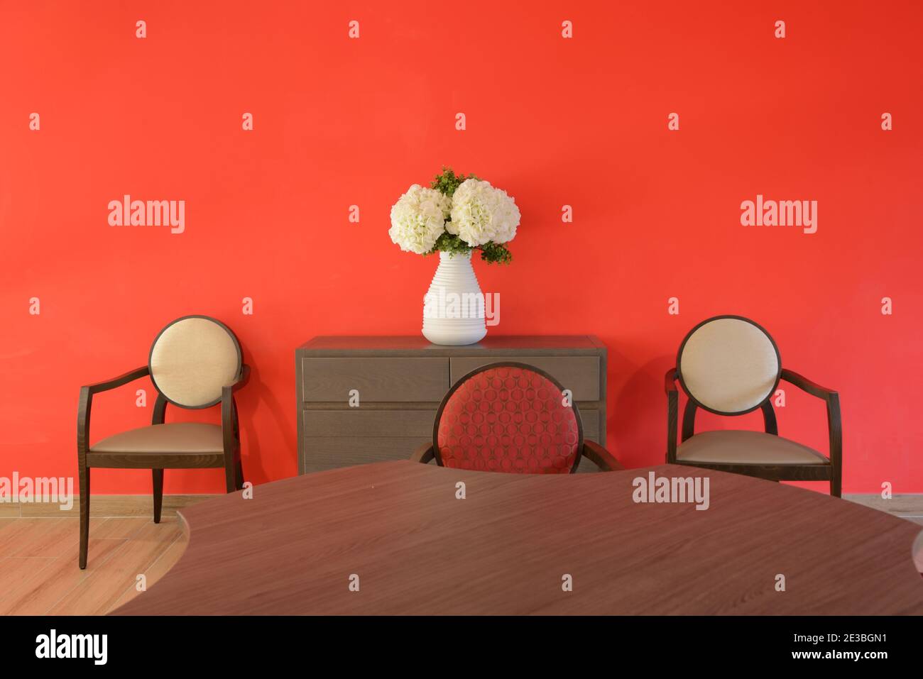 Sala da pranzo minimalista e contemporanea con tavolo da pranzo e pasti moderni Sedie fotografate contro una parete rossa Foto Stock