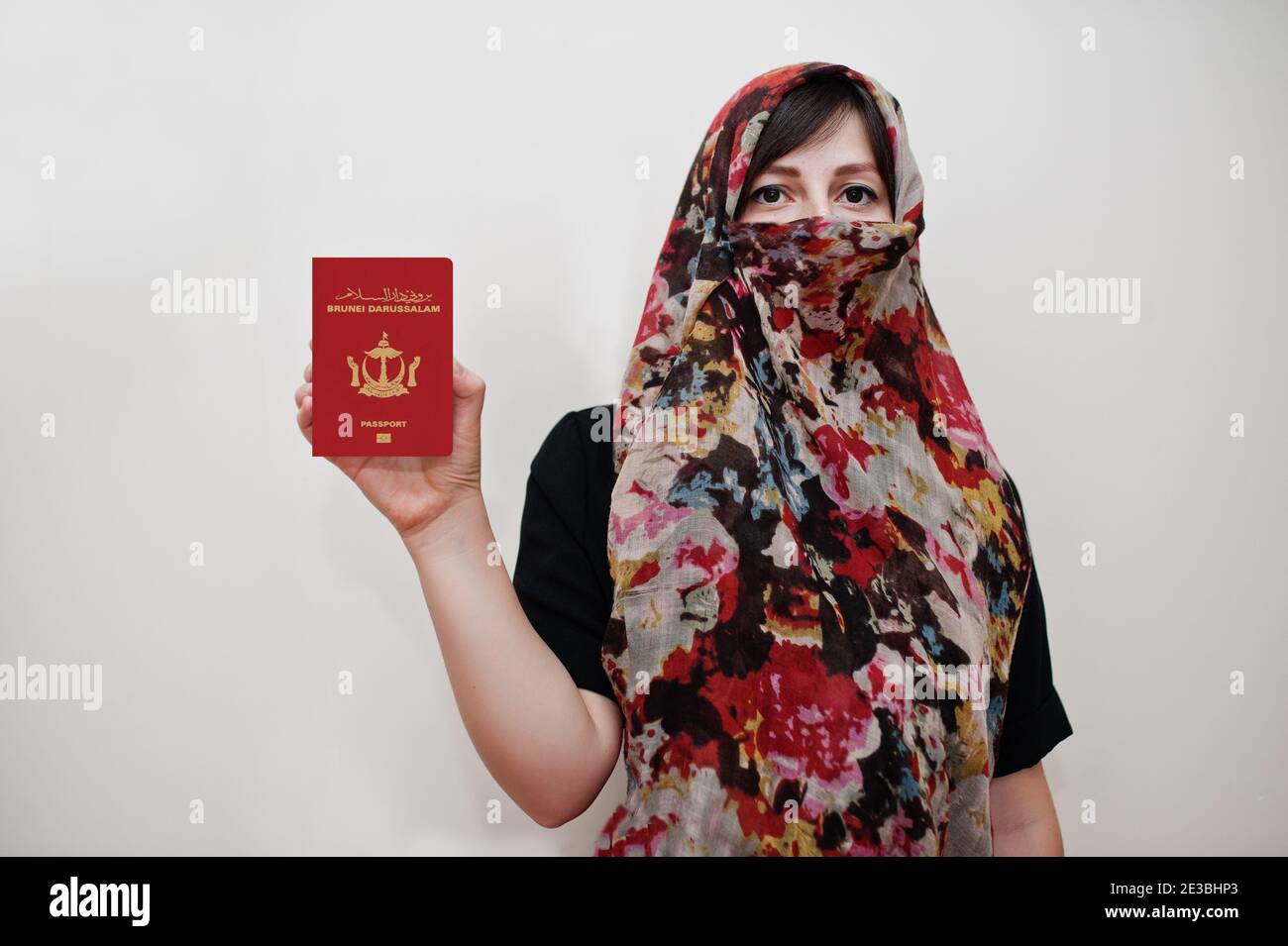 Giovane musulmana araba in abiti hijab tenere Nation of Brunei, l'Abode della Pace passaporto su sfondo bianco parete, studio ritratto. Foto Stock