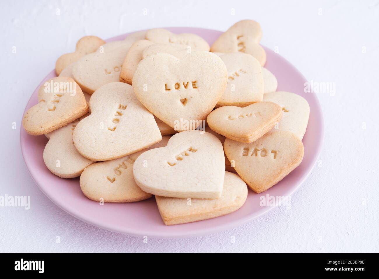 Piatto rosa con biscotti a forma di cuore e parola D'AMORE incisa. Concetto e amore per San Valentino. Foto Stock