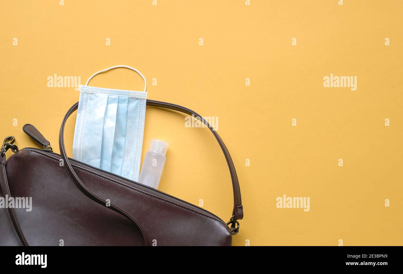 Custodia donna con maschera facciale e igienizzatore per le mani su sfondo giallo. Concetto di salute e sicurezza in movimento. Foto Stock