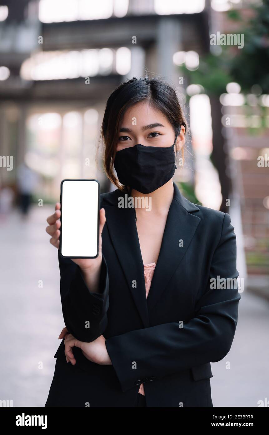 Ritratto di bella Businesswoman asiatica indossare maschera durante show mobile display del telefono con schermo bianco Foto Stock