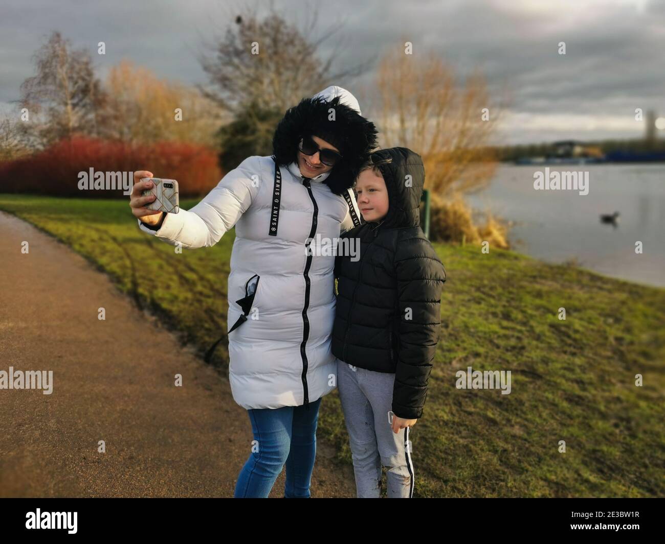 Una giovane madre prende un selfie con suo figlio come trascorrono del tempo all'aperto in una giornata fredda Foto Stock