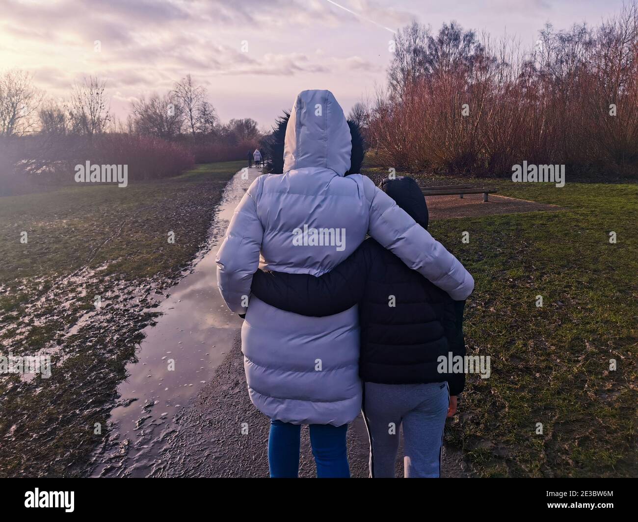 Madre e figlio si abbracciano mentre camminano attraverso un parco dopo che è stato allagato in una giornata fredda. Foto Stock