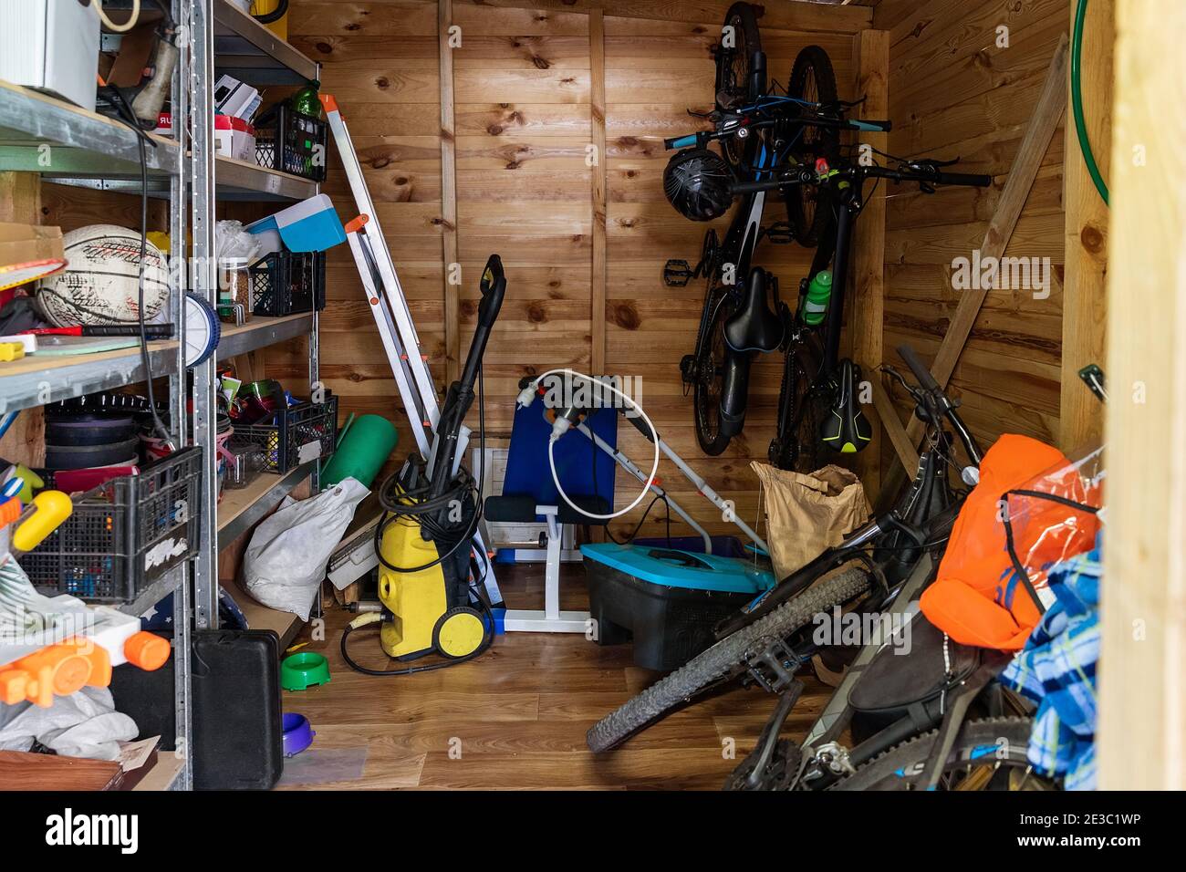 Unità di deposito di utilità di legno della casa suburbana con roba vario su mensole, biciclette, macchina di esercitazione, scala, attrezzi di giardino e attrezzatura. Disordinato Foto Stock