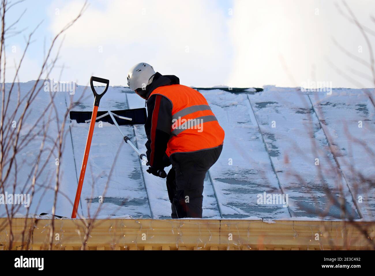 Lavoratore che rimuove la neve sul tetto di un edificio. Rimozione della neve, pulizia del tetto dell'arrampicatore in inverno Foto Stock