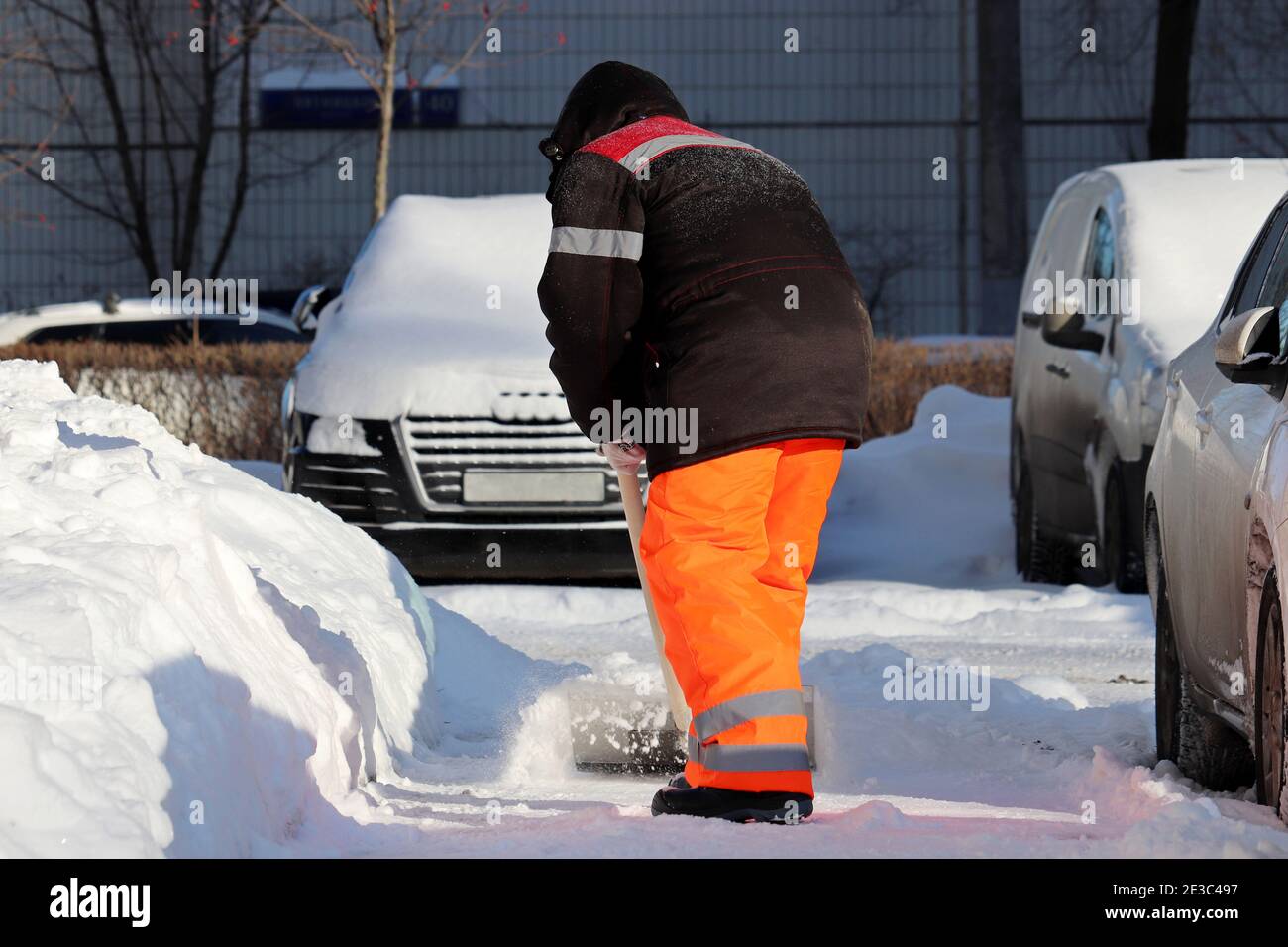 Rimozione della neve nella città invernale, pulizia della strada. Operaio in uniforme con una pala sul parcheggio Foto Stock