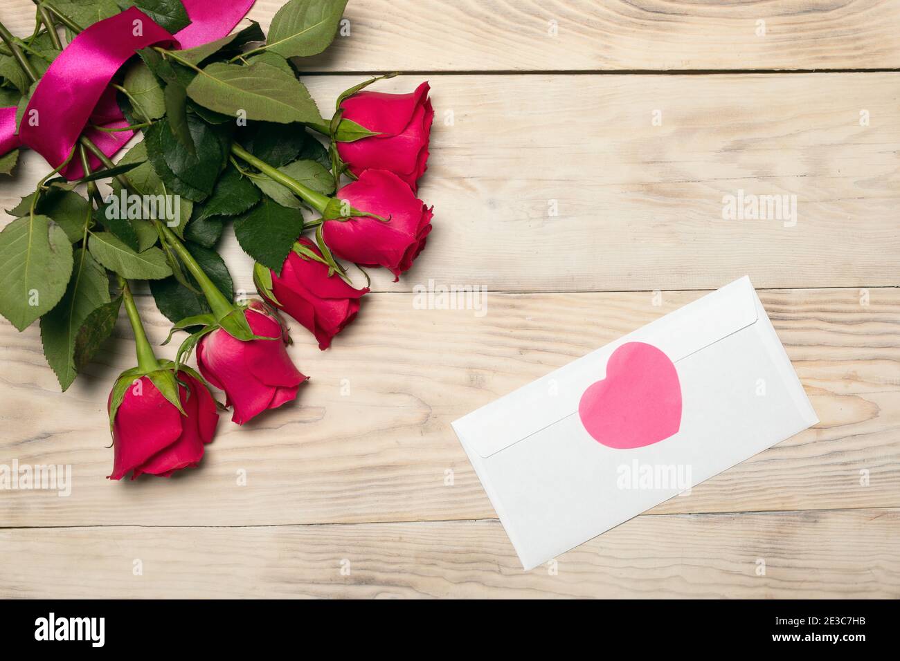 Rose rosse e cuore su sfondo ligneo, sopra, piatto. Modello di biglietto d'auguri romantico o invito. Foto Stock