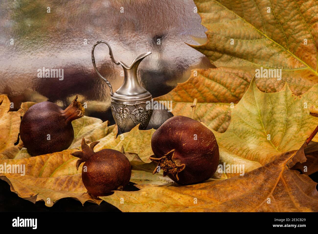 Ancora vita con foglie di sicomoro secche autunnali, melograni asciutti e caraffa decorativa da vicino su sfondo sfocato Foto Stock