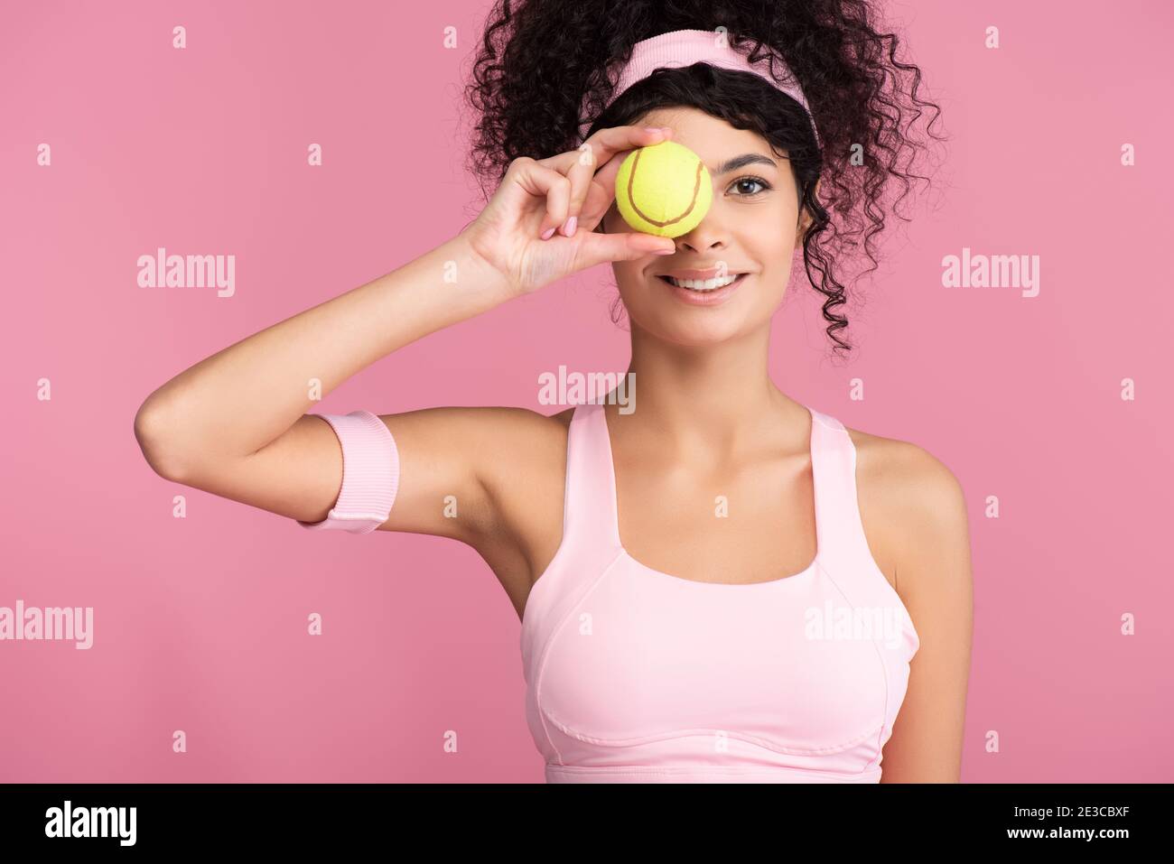 donna felice e sportiva che ricopre l'occhio con palla da tennis isolata su  rosa Foto stock - Alamy