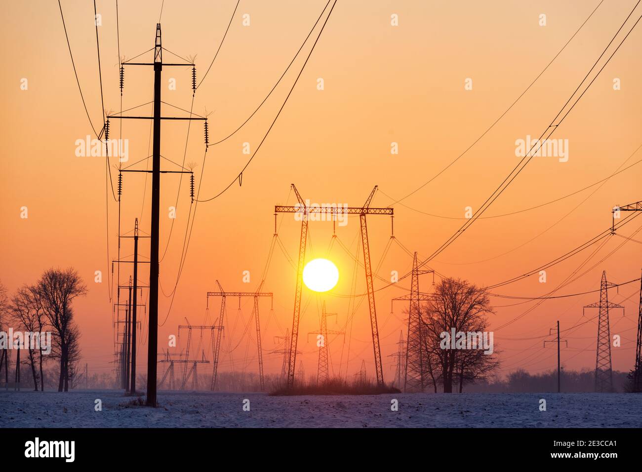Molte linee elettriche con tralicci e fili contro il sole che sale Foto Stock