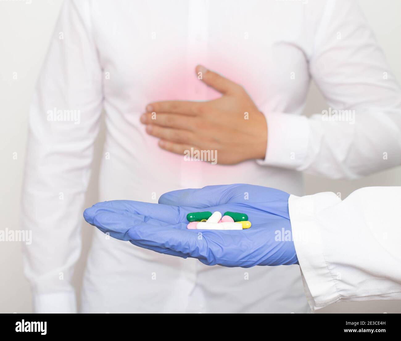 Il medico tiene le pillole in mano sullo sfondo di un uomo che tiene sullo stomaco per dolore e infiammazione nello stomaco. Il concetto o Foto Stock