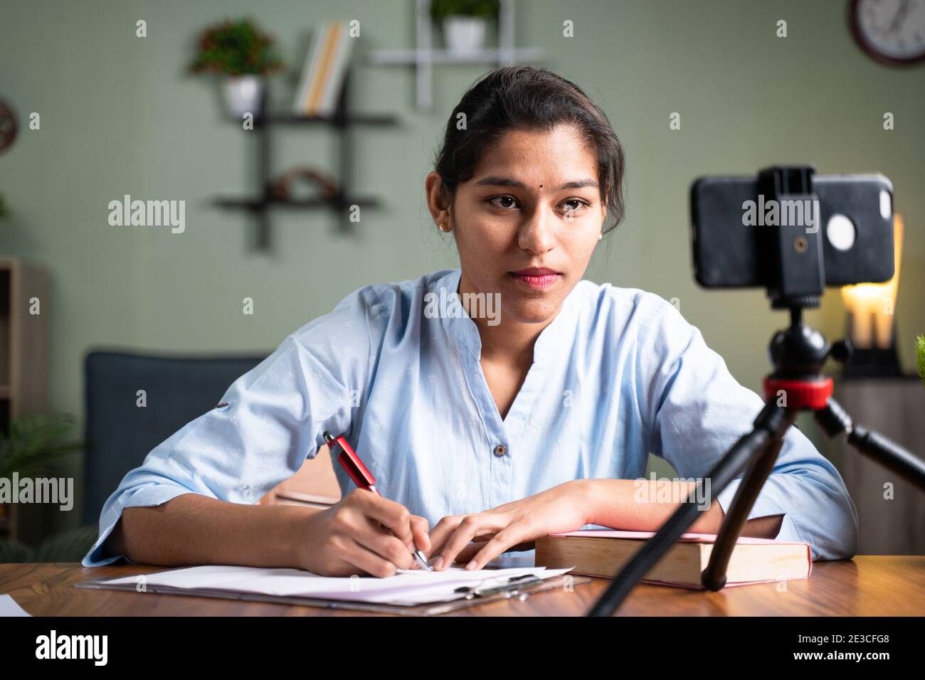 Giovane studente di ragazza dell'università che scrive le note guardando nel telefono mobile durante la classe in linea - concetto di nuovo normale, apprendimento virtuale, formazione in linea Foto Stock