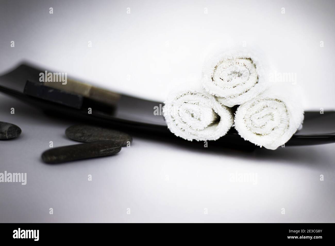Tre rotoli bianchi di asciugamani su un vassoio orientale nero e accanto a loro sapone nero e ciottoli di mare nero. Temi Spa. Foto Stock