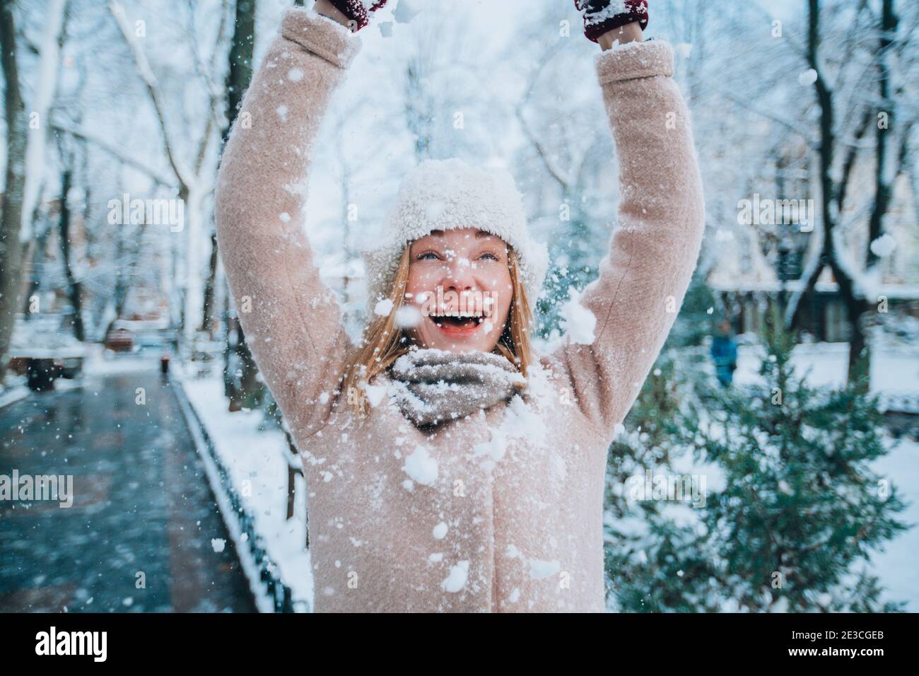 la giovane ragazza felice ride e getta la neve su se stessa. fiocchi di neve in primo piano Foto Stock