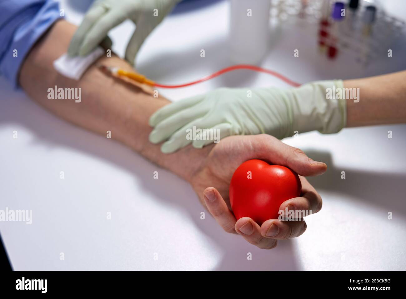 donazione di sangue - volontario donatore durante la donazione con un rosso cuore di gomma in mano Foto Stock