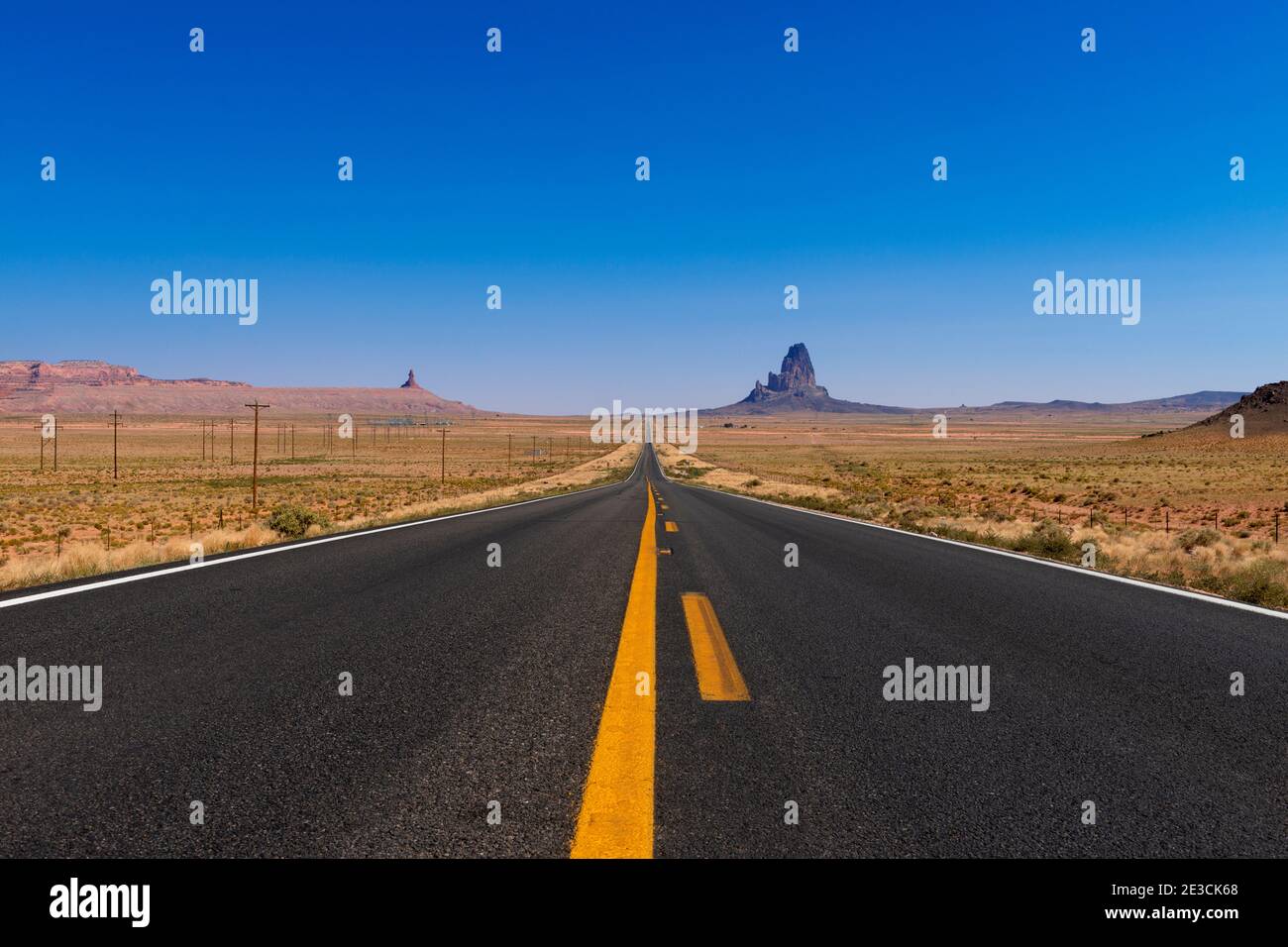 Vista panoramica dell'autostrada US 163 che conduce alla Monument Valley con i buttes in arenaria sullo sfondo; concetto di viaggio negli Stati Uniti e viaggio su strada. Foto Stock